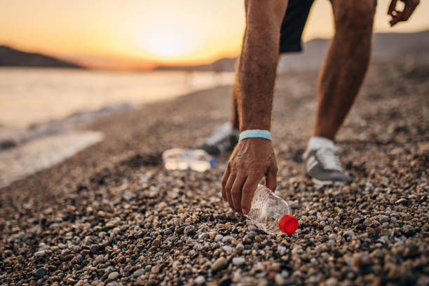 A mans hand picking up a plastic bottle at a beach clean