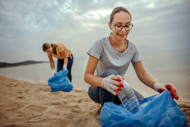 Two women collecing trash into bags at a beach